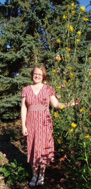 A woman standing next to a very tall sunflower